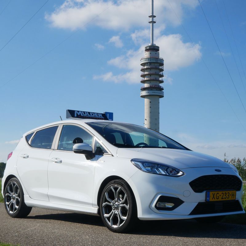 De witte Ford Fiesta ST-Line lesauto van Mulder Rijopleidingen met lesbord op het dak